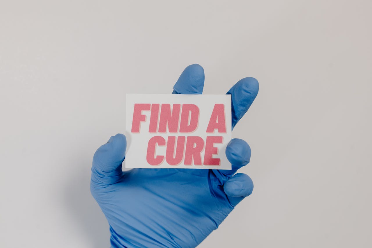 A blue-gloved hand holds a card with 'Find a Cure' message, symbolizing cancer awareness.
